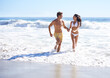 © Mapodile M./peopleimages.com - Holding hands, waves and happy couple running on beach for holiday adventure together on tropical island with care. Love, man and woman on ocean vacation with fun, romance and smile on travel in Bali