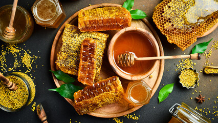 Honey banner. Honeycombs, honey in jars and flower pollen. On a black stone background