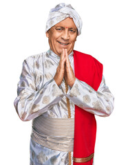 Wall Mural - Senior hispanic man wearing tradition sherwani saree clothes praying with hands together asking for forgiveness smiling confident.