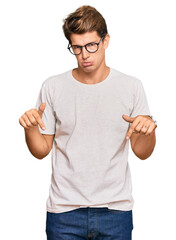 Wall Mural - Handsome caucasian man wearing casual clothes and glasses pointing down looking sad and upset, indicating direction with fingers, unhappy and depressed.