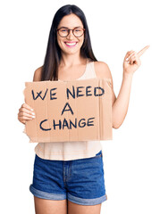 Poster - Young beautiful caucasian woman holding we need a change banner smiling happy pointing with hand and finger to the side