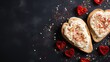  two pieces of bread with white frosting and red sprinkles on a black surface surrounded by hearts.