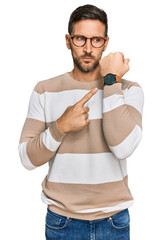 Canvas Print - Handsome man with beard wearing casual clothes and glasses in hurry pointing to watch time, impatience, looking at the camera with relaxed expression