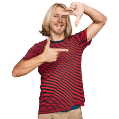 Poster - Caucasian man with blond long hair wearing casual striped t shirt smiling making frame with hands and fingers with happy face. creativity and photography concept.