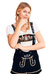 Wall Mural - Young beautiful blonde woman wearing oktoberfest dress looking confident at the camera smiling with crossed arms and hand raised on chin. thinking positive.