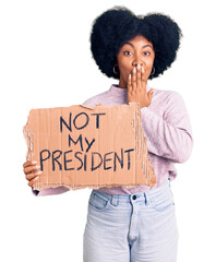 Poster - Young african american girl holding not my president protest banner covering mouth with hand, shocked and afraid for mistake. surprised expression