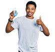 © Krakenimages.com - Young african american man holding glucometer device smiling happy and positive, thumb up doing excellent and approval sign
