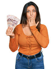 Canvas Print - Beautiful hispanic woman holding mexican pesos covering mouth with hand, shocked and afraid for mistake. surprised expression