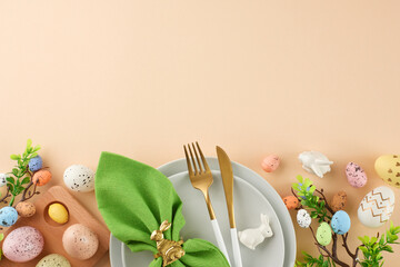 Wall Mural - Easter traditions unfold in the dining presentation. Top view shot of plates, eggs, cutlery, green napkin, ceramic bunnies, green branches on beige background with empty space for festive message