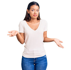 Wall Mural - Young beautiful latin girl wearing casual white t shirt clueless and confused expression with arms and hands raised. doubt concept.