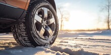 Close up of car tire stands in the snow in winter, the sun shines from behind the wheel 