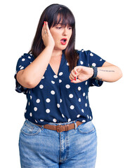 Poster - Young plus size woman wearing casual clothes looking at the watch time worried, afraid of getting late