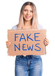 © Krakenimages.com - Young beautiful blonde woman holding fake news banner looking positive and happy standing and smiling with a confident smile showing teeth