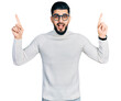 © Krakenimages.com - Young arab man with beard wearing elegant turtleneck sweater and glasses smiling amazed and surprised and pointing up with fingers and raised arms.