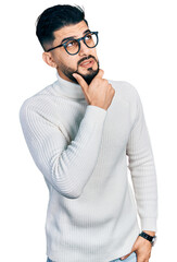 Wall Mural - Young arab man with beard wearing elegant turtleneck sweater and glasses thinking worried about a question, concerned and nervous with hand on chin