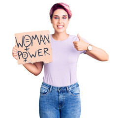 Sticker - Young beautiful woman with pink hair holding woman power banner smiling happy and positive, thumb up doing excellent and approval sign