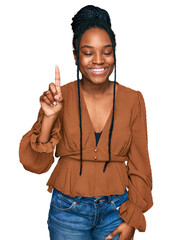 Wall Mural - Young african american woman wearing casual clothes showing and pointing up with finger number one while smiling confident and happy.