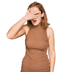 Wall Mural - Young caucasian woman wearing casual clothes peeking in shock covering face and eyes with hand, looking through fingers with embarrassed expression.