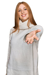 Wall Mural - Young irish woman wearing casual winter sweater smiling cheerful offering palm hand giving assistance and acceptance.