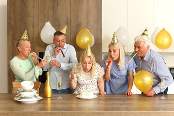 Poster - Mature woman with her friends making wish at Birthday party in kitchen