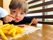 Cute little caucasian boy eating fries in fast food restaurant. Little child eats junk food straight from the table with some ketchup.