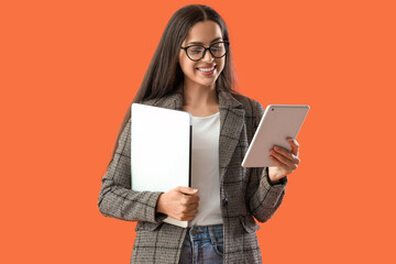 Pretty young female programmer with laptop and tablet computer on orange background