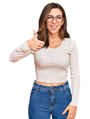 Wall Mural - Young brunette woman wearing casual clothes and glasses doing happy thumbs up gesture with hand. approving expression looking at the camera showing success.