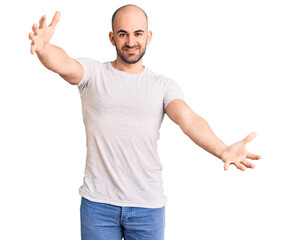 Sticker - Young handsome man wearing casual t shirt looking at the camera smiling with open arms for hug. cheerful expression embracing happiness.