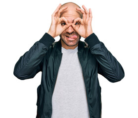 Poster - Young hispanic man wearing casual clothes doing ok gesture like binoculars sticking tongue out, eyes looking through fingers. crazy expression.