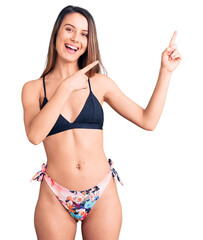 Wall Mural - Young beautiful girl wearing bikini smiling and looking at the camera pointing with two hands and fingers to the side.