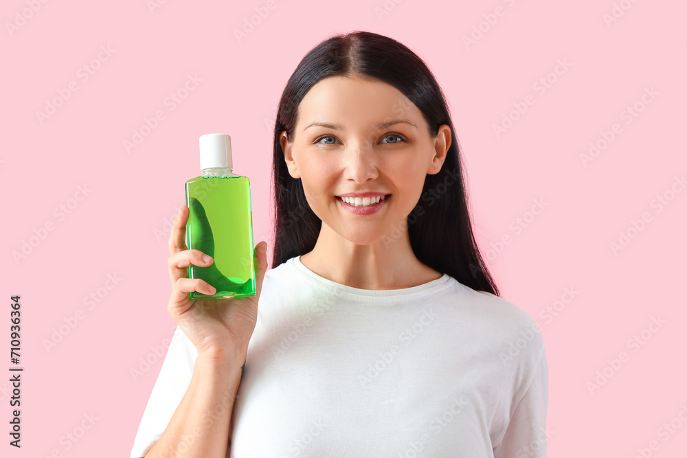 Smiling young woman with mouth rinse on pink background