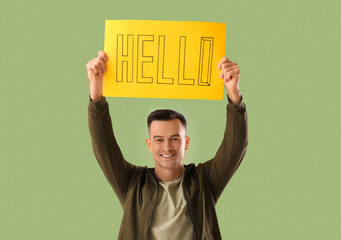 Canvas Print - Handsome man holding paper with word HELLO on green background