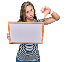 Young Blonde Woman Holding Empty White Board With Angry Face, Negative Sign Showing Dislike With Thumbs Down, Rejection Concept