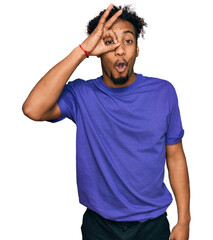 Wall Mural - Young african american man with beard wearing casual purple t shirt doing ok gesture shocked with surprised face, eye looking through fingers. unbelieving expression.