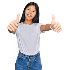 Wall Mural - Beautiful young asian woman wearing casual white t shirt approving doing positive gesture with hand, thumbs up smiling and happy for success. winner gesture.