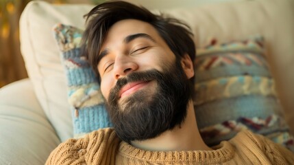 Handsome young man with black hair and beard sleeping on a pillow and smiling, relaxing on the couch or sofa. Closeup male model wearing yellow sweater, attractive guy at home or house