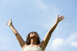 Beautiful Spanish brunette woman with long curly hair raises her arms to the blue sky. The woman is happy and thanks god and life for every day. Concept happiness and thankfulness.