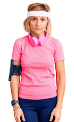 Poster - Young blonde woman wearing sportswear and headphones with serious expression on face. simple and natural looking at the camera.