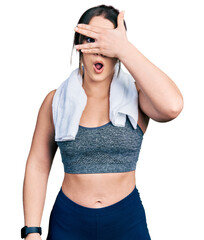 Wall Mural - Young hispanic girl wearing sportswear and towel peeking in shock covering face and eyes with hand, looking through fingers with embarrassed expression.