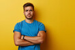© v.senkiv - Sad tanned handsome man in blue t-shirt thinking about problems at work, folding his arms, posing isolated on yellow background of studio. Copy space Banner layout. People's emotions Lifestyle concept
