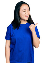 Wall Mural - Young chinese woman wearing casual blue t shirt pointing thumb up to the side smiling happy with open mouth