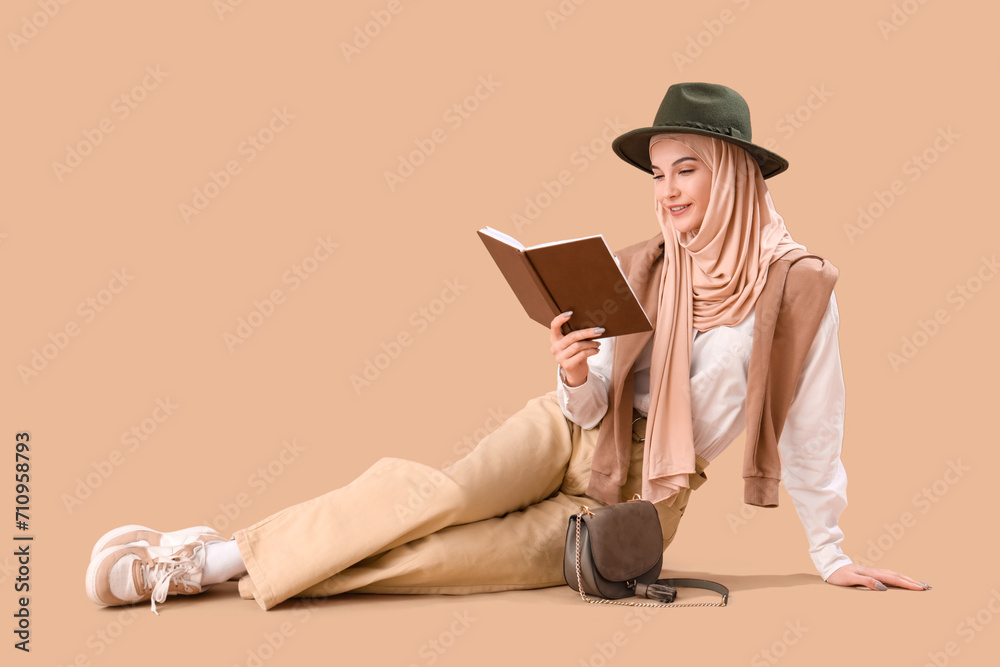 Stylish Muslim woman reading book on brown background