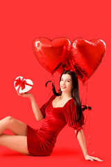 Sticker - Beautiful young woman with heart-shaped air balloons and gift for Valentine's day on red background