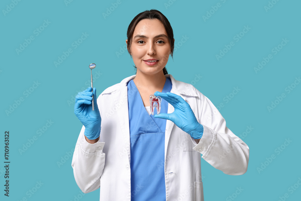 Young female dentist with dental mirror and tooth model on blue background