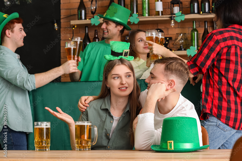 Young couple with beer celebrating St. Patrick's Day at table in pub