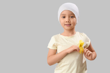 Sticker - Cute little Asian girl after chemotherapy with yellow ribbon on grey background. Childhood cancer awareness concept