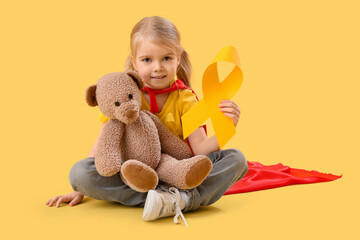 Canvas Print - Cute little girl in superhero costume with yellow ribbon and teddy bear on color background. Childhood cancer awareness concept