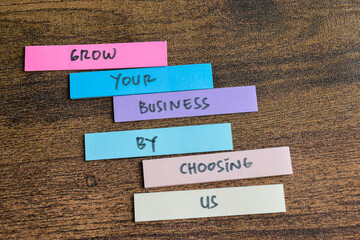 Wall Mural - Concept of Grow Your Business by choosing us write on sticky notes isolated on Wooden Table.