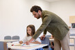 © zinkevych - Man primary school teacher in classroom with girl pupil.