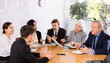 © JackF - Focused colleagues of different ages sitting around the table and talking before working day in office
